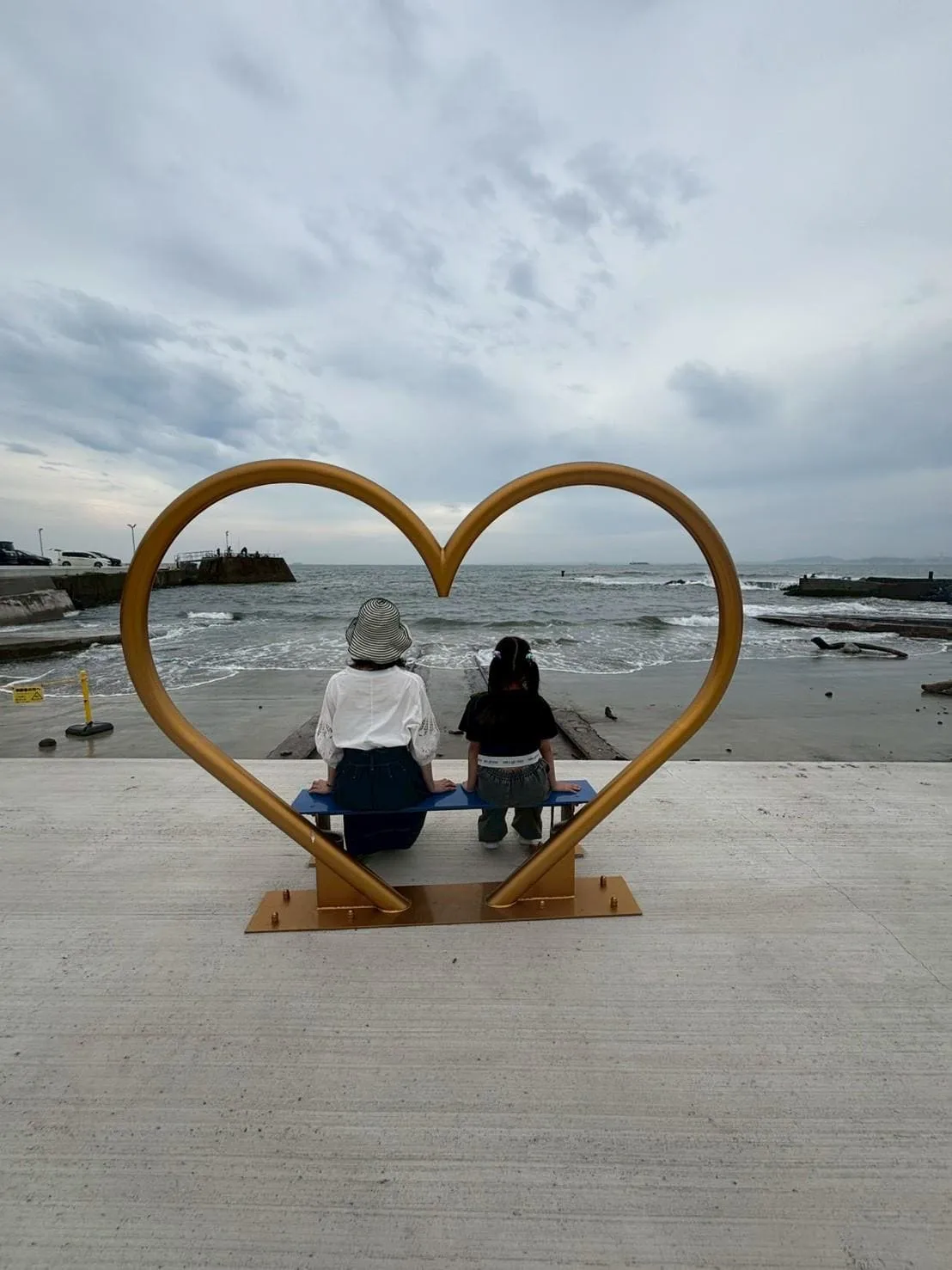 ハートのベンチに座って海を眺める親子